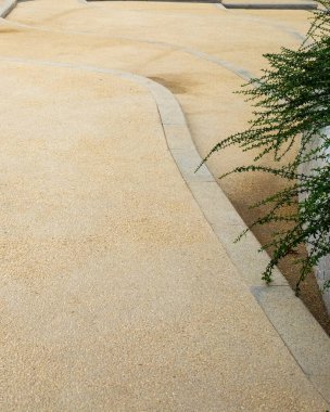 Üzerinde kıvrımlı çizgiler ve yeşil bitkiler olan sarı asfalt bir yüzey. Görüntü, soyut doku ve peyzaj yolu tasarımını iletir. Yüksek kaliteli gerçek fotoğrafçılık..