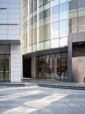 Camdan duvarlar ve güneş ışığı ve gölgeli asfalt bir plazanın bulunduğu modern bir ticari ofis binasının girişi. İmaj profesyonelliği ve kentsel mimariyi yansıtıyor. Yüksek kaliteli gerçek fotoğrafçılık..