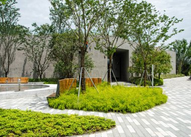 Peyzaj bahçesiyle çevrili modern bir minimalist beton bina girişi. Kavisli kaldırım yolu, taze yeşil zemin örtüsü ve genç ağaçlar temiz ve çağdaş bir mimari ortam yaratıyor..