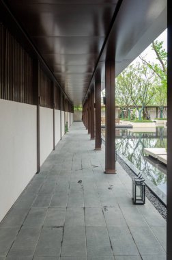 Modern Asya tarzı bir bahçede kapalı bir koridor ya da koridorun dikey perspektifli görüntüsü. Karanlık sütunlar, ahşap bir çatı ve taş zemin yapılandırılmış ve huzurlu bir mimari yol yaratır..