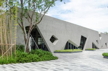 HANGZHOU, ÇİN - 3 Temmuz 2017: Eşsiz düzensiz elmas şekilli pencereleri olan gri desenli ön cepheli bir yerleşim yerindeki modern bir binanın dış görünüşü. Bambu ve çalılar mimariyi çerçeveler..