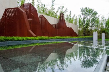 HANGZHOU, ÇİN - 3 Temmuz 2017: Paslı çelikten yapılmış soyut bir dağ heykelinin manzaralı görüntüsü, bir bahçe havuzunun sakin sularına mükemmel bir şekilde yansıyor. Tasarım endüstriyel materyalleri doğa temalarıyla birleştirir..