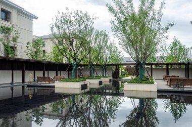 HANGZHOU, ÇİN - 4 Temmuz 2017: Üst düzey bir topluluktaki manzaralı bir su bahçesi manzarası. Tasarımda, modern Asya estetiğine örnek olarak havuz içindeki kare ağaç ekicileri ve ahşap koridorlar yer alıyor..