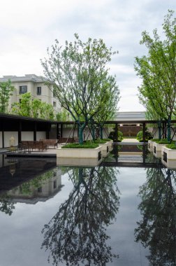 HANGZHOU, ÇİN - Temmuz 04, 2017: simetrik modern Çin avlusunun dikey çekimi. Merkezde dikilen ağaçlar, yerleşim yerleri ve koridorlarla çevrili karanlık ve durgun su havuzuna mükemmel bir şekilde yansıyor..