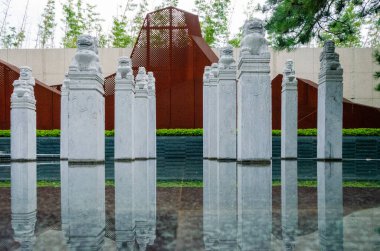 HANGZHOU, ÇİN - 3 Temmuz 2017: Paslı, dağ şeklinde bir ekranın önündeki su havuzunda geleneksel taş direkleri gösteren simetrik bir manzara. Bambu ve çam ağaçları bileşimi çerçeveler.