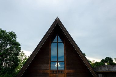 HANGZHOU, ÇİN - 06 Temmuz 2017: Bulutlu bir gökyüzüne karşı Meilizhou Kilisesi 'nin üçgen çatısının üst kısmının detaylı bir çekimi. Ahşap yapı ve büyük cam haç penceresi açıkça görülüyor..