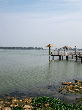 WUHAN, Çin - 19 Ekim 2016: Doğu Gölü 'nün yeşil sularına uzanan ahşap bir izleme platformu. Sahne, Çin 'in en büyük kentsel gölünün sakin su ortamını ve uzak ufkunu yakalıyor..