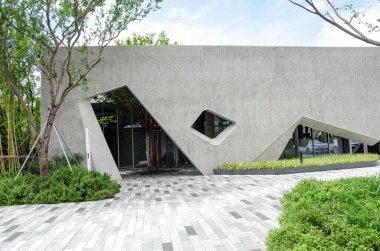 HANGZHOU, ÇİN - 3 Temmuz 2017: Geometrik pencere kesiklerini ve gri taş kaplamaları gösteren modern bir kamu binasının ön cephesine daha yakından bakmak. Yeşil ağaçlar ve manikürlü çalılar ön tarafı süslüyor..