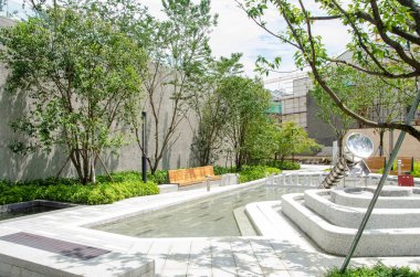 HANGZHOU, ÇİN - 3 Temmuz 2017: Sığ su havuzu, taş basamaklar ve yeşil ağaçların yer aldığı modern bir yerleşim bölgesinde bir açık hava eğlence alanı. Sağda bir metal kayması veya heykel görülebilir..