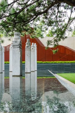 HANGZHOU, ÇİN - 3 HAZİRAN 2017: Su yüzeyine yansıyan oyulmuş taş kolonların dikey yakın çekimi. Arka planda paslı kırmızı Corten çelik bir duvar, eski ve yeni malzemeler arasında bir kontrastlık yaratır.