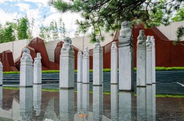 HANGZHOU, ÇİN - 3 Temmuz 2017: Yansıtıcı su havuzunda duran bir sıra geleneksel taş bağlanma direklerinin yer aldığı bir peyzaj. Çam dalları ve paslı çelik zemin modern Zen estetiğini tamamlıyor..