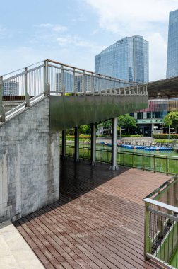 HANGZHOU, ÇİN - 05 Temmuz 2017: Hangzhou 'daki modern gökdelenlere ve nehir kıyısına bakan bir köprü altındaki ahşap gözlem güvertesine bakın. Sahne, kanal boyunca kentsel gelişimi yakalıyor..