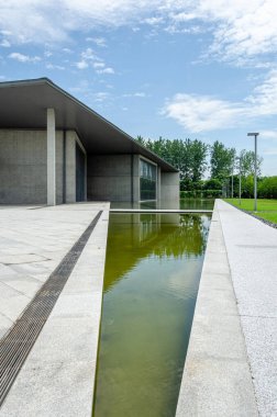 HANGZHOU, ÇİN - 06 Temmuz 2017: Liangzhu Sanat Merkezi 'nde sığ bir su havuzu ve geometrik beton duvarların dikey çekimi. Tasarım, sakin su elementlerini keskin Brutalist mimari çizgilerle birleştiriyor..