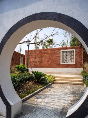 Geleneksel Çin dairesel taştan ay kapısından bak. Kırmızı tuğla duvar ve yeşil bahçe yolu..