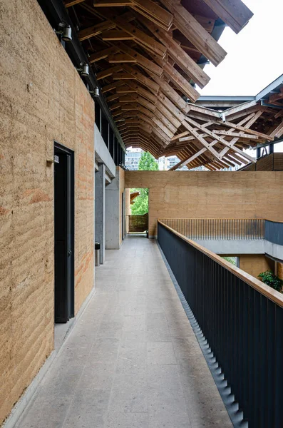Solda dokulu dünya duvarları olan yarı açık hava koridorunun dikey görüntüsü. Yukarıda, karmaşık ve karmaşık bir ahşap çatı yapısı modern mimari bağlamda geleneksel işçiliği gösteriyor..