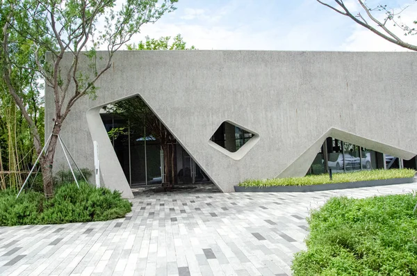 HANGZHOU, ÇİN - 3 Temmuz 2017: Geometrik pencere kesiklerini ve gri taş kaplamaları gösteren modern bir kamu binasının ön cephesine daha yakından bakmak. Yeşil ağaçlar ve manikürlü çalılar ön tarafı süslüyor..