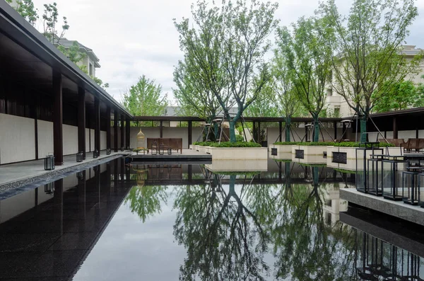 HANGZHOU, ÇİN - 4 Temmuz 2017: Çevredeki ağaç ve binaları yansıtan büyük ve sakin bir su havuzunun yer aldığı lüks bir konutun geniş bir manzarası. Tasarım simetriyi ve barışı vurguluyor..