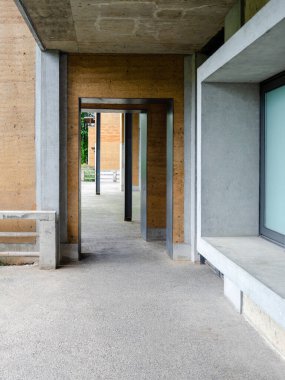 Çerçeve içinde geometrik bir çerçeve oluşturan beton sütunlar ve dokulu duvarlarla modern bir mimari koridorun perspektif görüntüsü.