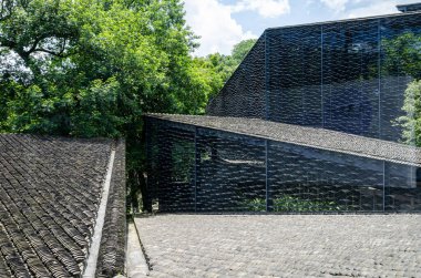 Tel örgüye asılmış gri kiremitlerden oluşan, yeşil ağaçlarla harmanlanmış eşsiz bir modern binanın yüksek açılı görüntüsü..