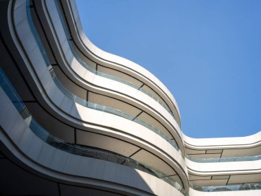 Beyaz eğimli balkonları ve açık mavi gökyüzüne karşı cam pencereleri olan modern gelecekçi mimarinin düşük açılı görüntüsü.