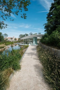 Qinhuangdao, Hebei Eyaleti, Çin - 16 Eylül 2018: Çakıl yolunun dikey perspektifi uzun çimenler ve bitkiler arasından modern bir pavyona doğru ilerliyor.