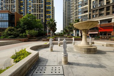 Çağdaş bir apartman kompleksinin avlusunda, su bulunmayan taş çeşme havzası ve heykel elementlerinin ayrıntıları.