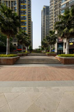 Dikey bileşim, palmiye ağaçlarıyla kaplı kaldırım ve merdivenleri gösteriyor. Mavi gökyüzüne karşı yükselen modern apartman binalarına bakıyor..