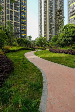 Yeşil çimleri kesen sarmal tuğla yolunun dikey görüntüsü arka plandaki yüksek apartman binalarına doğru gidiyor..