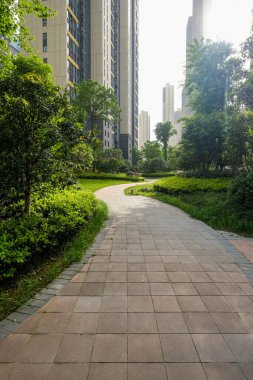 Olgun ağaçların ve yeşilliklerin arasında kıvrılarak, modern bir apartman kompleksi içinde gölgeli bir yol sağlayan, huzurlu bir kaldırım geçidi..