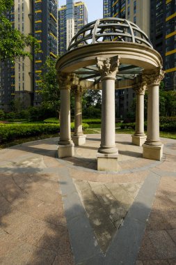 Klasik taş bir çardağın tam dikey görüntüsü sütunları ve kubbeli çatısı modern yerleşim yerinin bahçesinde asfalt bir yüzey üzerinde duruyor..