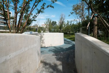 Kavisli beton istinat duvarlarının mimari ayrıntıları ve modern bir şehir parkında kaldırım ya da kaykay parkı, ağaçlar ve mavi gökyüzü ile çevrili..