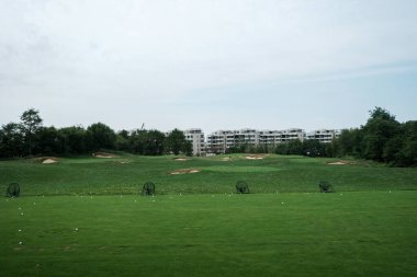 Geniş açılı, yemyeşil golf sahasının yatay manzarası. Uzakta ağaçlar ve binalar olan dağınık beyaz golf toplarıyla kaplı..
