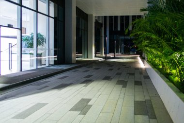 Camdan duvarları, aydınlık yolları ve yeşil peyzajı olan modern bir ticari binanın gece manzarası..