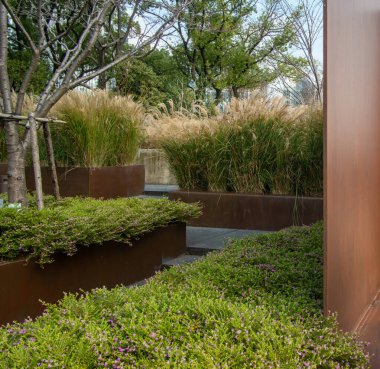 Paslı korse çelik istinat duvarlarının bulunduğu modern bir bahçenin köşesi yeşil çalılar ve bir ağacın yanında süslü otlar için ekici görevi görüyor..