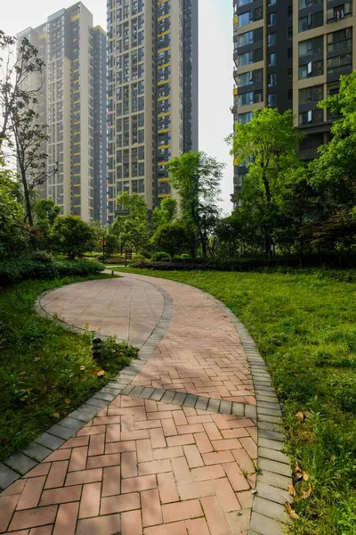 Yuvarlak kırmızı tuğlalı bir geçitin dikey görüntüsü yeşil bir çimenliğin içinden geçip modern yüksek katlı apartmanlara doğru gidiyor..