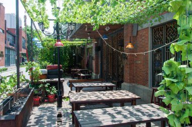 Wuhan, Hubei Eyaleti, Çin - 7 Haziran 2017: Hankou 'da kırmızı tuğlalı bir binanın yanındaki yeşil yaprakların ve sarmaşıkların altındaki ahşap masalı boş bir açık hava oturma alanı.