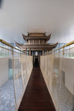 Mükemmel merkezli geniş açı perspektifi geleneksel ahşap bir pavyon heykelini modern bir yapı koridoruna örgülü parmaklıklar ile entegre ediyor..