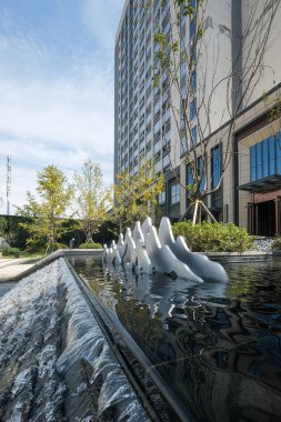 Beyaz bir heykel ile katmanlı bir su çeşmesinin dikey çekimi modern bir ofis binası ve mavi gökyüzü üzerine kuruludur..