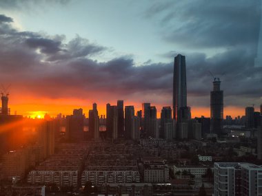 Wuhan, Hubei Eyaleti, Çin - 01 Ağustos 2024: Yoğun turuncu gün batımı Wuchang semtindeki gökdelenlerin ve konut binalarının arkasında güneş ışığı ufukta parlıyor.