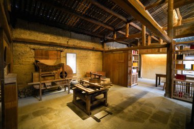 Açığa çıkmış ahşap yapılar, geleneksel aletler ve sıcak ortam aydınlatmasının yer aldığı tarihi bir zanaat atölyesinin kapalı bir perspektifi.