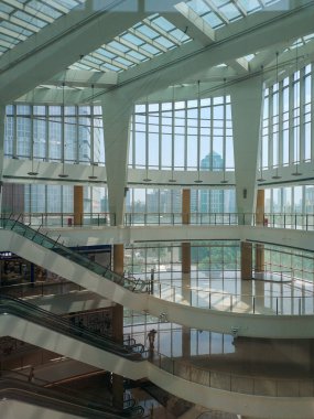 Geniş cam tavan, çelik yapılar ve modern yürüyen merdivenlerin yer aldığı çok katlı çağdaş bir alışveriş merkezinin iç perspektifi..