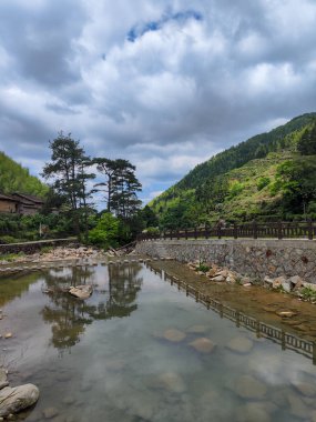 Bereketli bir dağ vadisini ve bulutlu gökyüzünü yansıtan sakin bir nehir nehri. Nehir boyunca geleneksel taş duvarlar var..