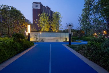 Parktaki canlı mavi koşu yolunun alacakaranlık görüntüsü, modern ayakta duran aydınlatmalarla aydınlatılıyor..