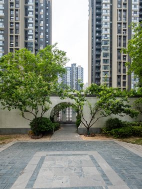 Geleneksel yuvarlak taş kemer yoluyla dikey bir manzara manikürlü bir bahçe alanına, ağaçlar ve yüksek katlı dairelerle çerçevelenmiş.
