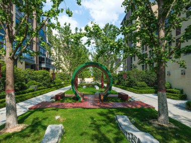 Çağdaş bir apartman bahçesindeki ağaçlar ve yeşil çimlerle çevrili asfalt bir geçitteki dairesel ahşap kapı yapısının manzarası..