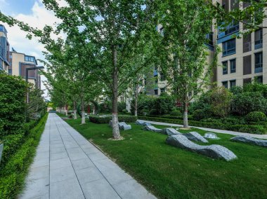 Modern apartman binaları arasında yer alan taştan yollar ve doğal taş koltuklu iyi korunmuş bir bahçe manzarası..