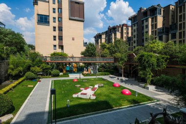 Manikürlü geometrik çimenlik bölümleri, kırmızı dekoratif aksanları ve apartman binaları olan bir avlu manzarası..