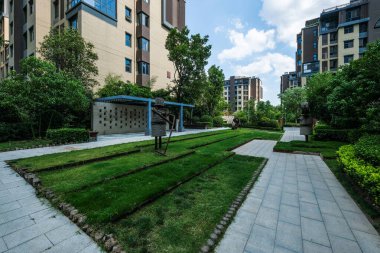 Taştan yollar, yeşil çimenler ve konut binalarıyla çevrili ince su elementinin yer aldığı modern bir bahçe manzarası..