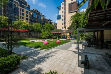 Geniş yürüyüş yolları, yeşil çimenler ve açık mavi gökyüzü altında kırmızı dekoratif heykellerin yer aldığı bir apartman manzarası..