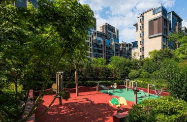 Çocuklar için parlak ve neşeli bir oyun parkı manzarası, bir apartman parkındaki yemyeşil ağaçların arasında yer alıyor..